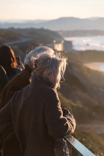 Personne âgée appuyée sur la rambarde, contemplant la côte au coucher du soleil
