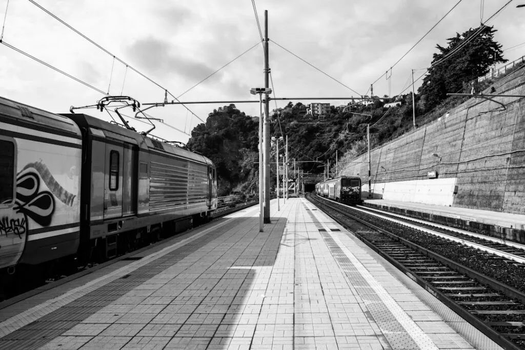 Gare ferroviaire de Cinque Terre, quais vides et train sous caténaires en noir et blanc