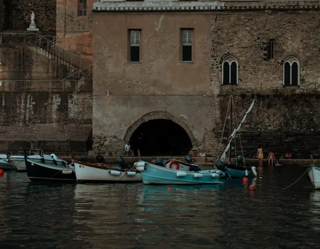 Petits bateaux amarrés devant un mur de pierre et arche, Vernazza.