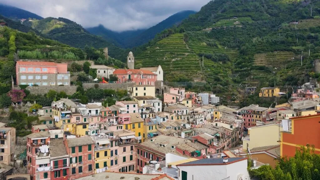 Pastelkleurige huizen tegen terrassen en bergen in een Cinque Terre-dorp
