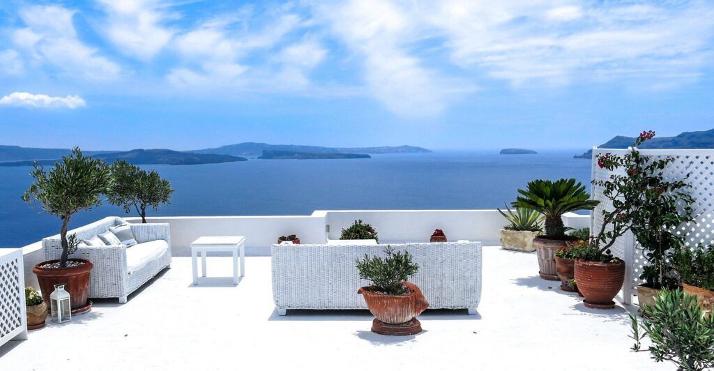 White terrace with wicker seating and potted plants overlooking the sea