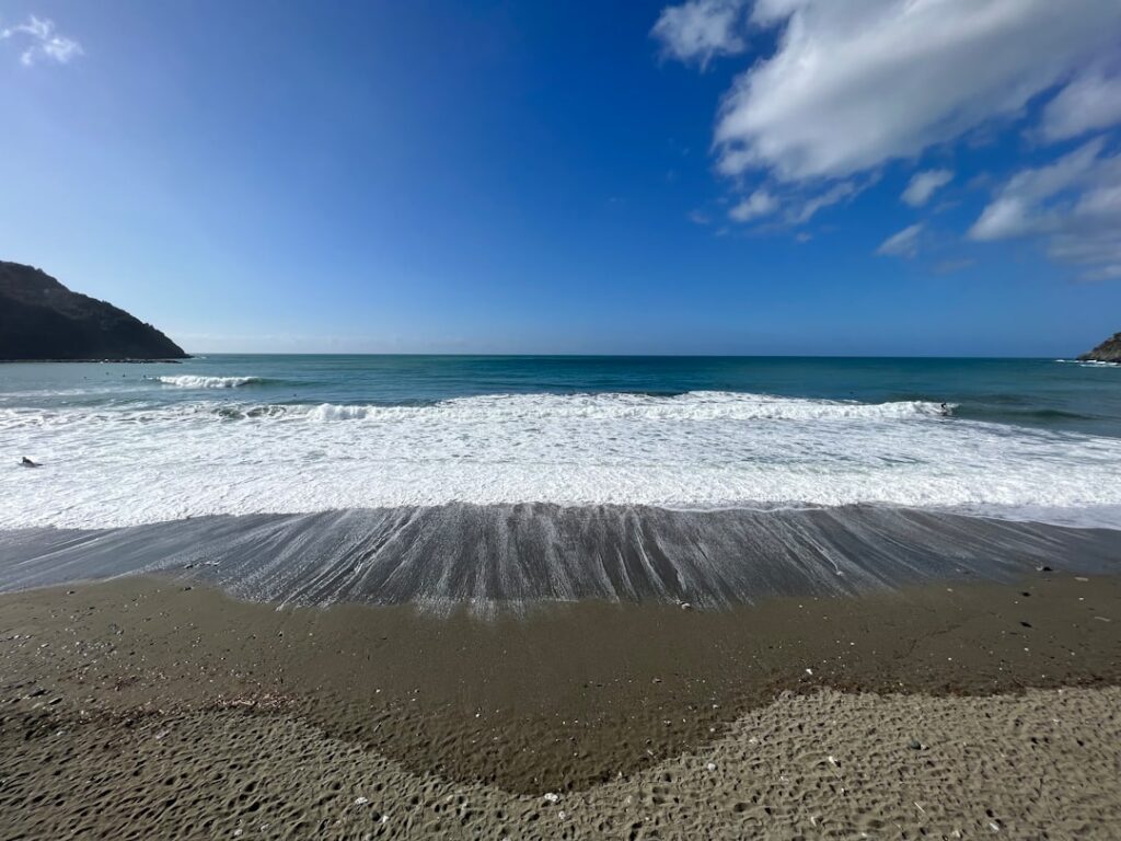 Wide sandy shoreline with incoming waves under a blue sky in Cinque Terre