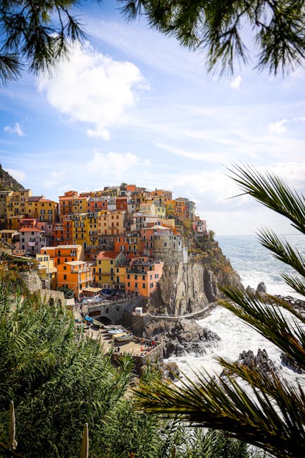 Palm-framed view of Cinque Terre houses clinging to seaside cliffs.