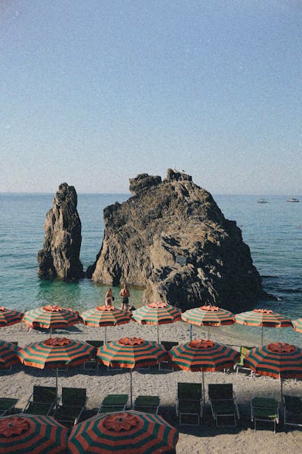 Grand rocher marin devant parasols rayés orange et vert à Cinque Terre