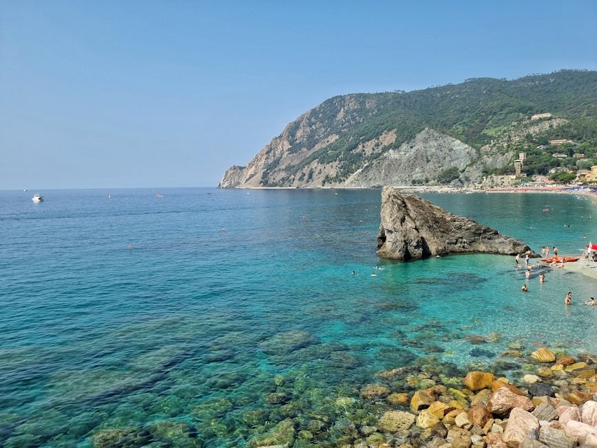Turquoise Cinque Terre water with rocky shoreline and sunbathers.