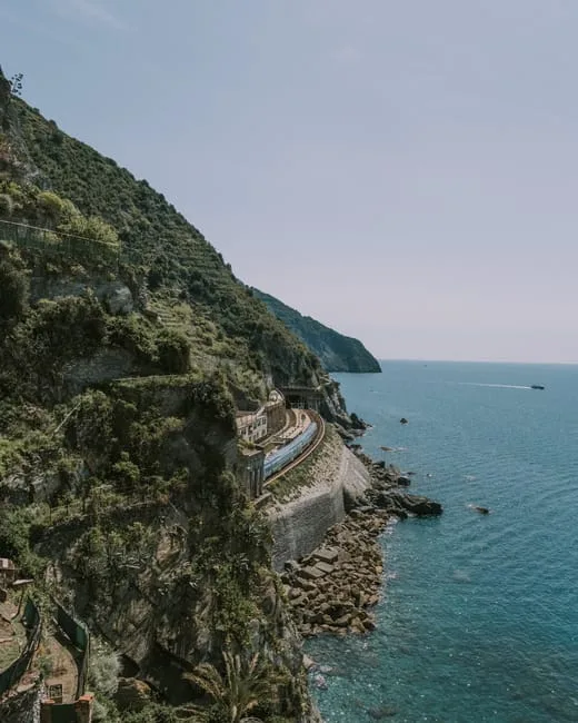 Trein rijdt langs rotsachtige kustlijn boven blauwe zee in Cinque Terre