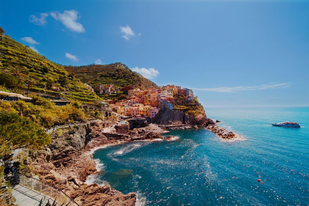 Bright sunlit Cinque Terre cliff village with terraced vineyards and boat