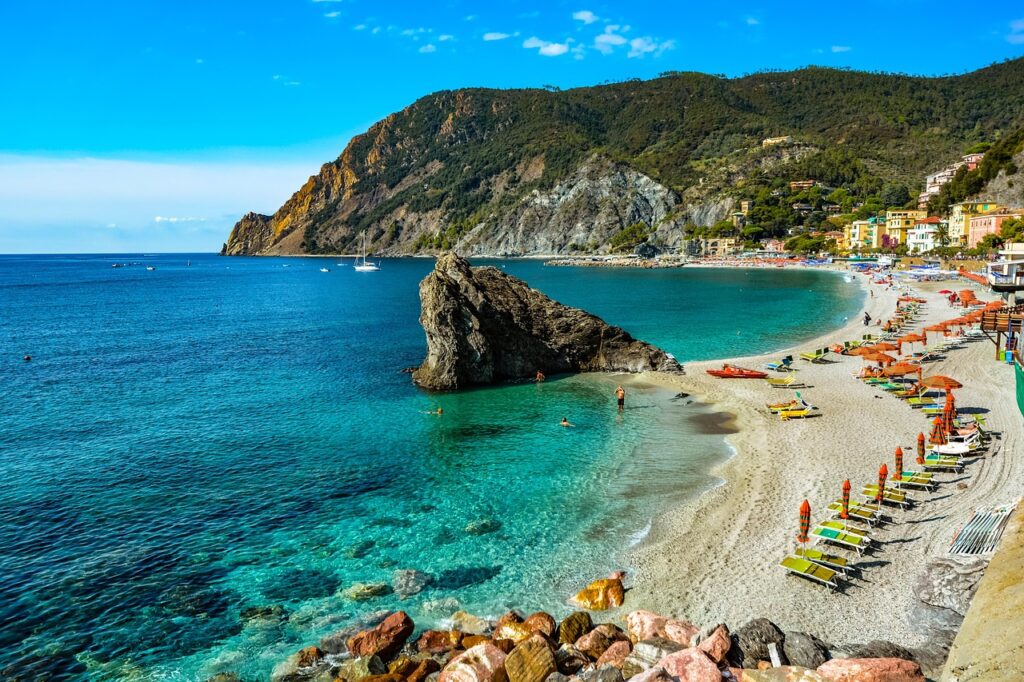 Turquoise sea at Cinque Terre beach with large rock and loungers
