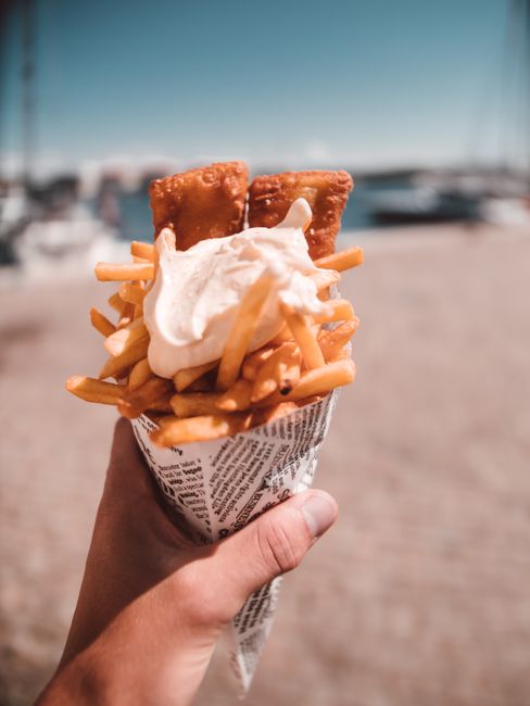 Hand hält Papiertüte mit Fish & Chips auf der Straße in London