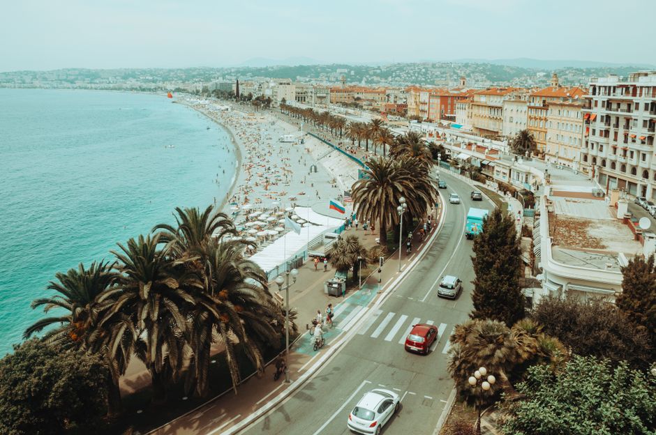 Brede boulevard met palmbomen en strand langs de Promenade des Anglais