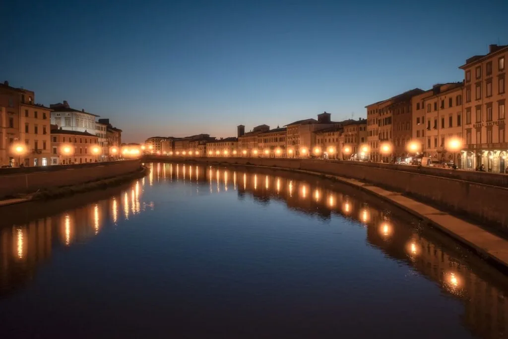 Oświetlone nabrzeże Arno z odbiciami lamp nocą w Pizie