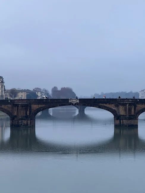 Mglista panorama kamiennego mostu nad Arno ze sylwetkami przechodniów w Pizie.