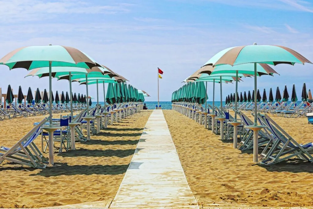 Piaszczysta plaża z równymi rzędami turkusowych parasoli i leżaków