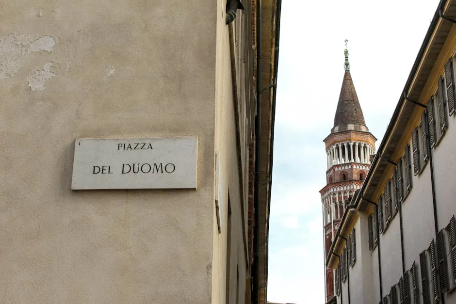 Tablica 'Piazza del Duomo' przy wąskiej ulicy, widoczna wieża w Pizie.
