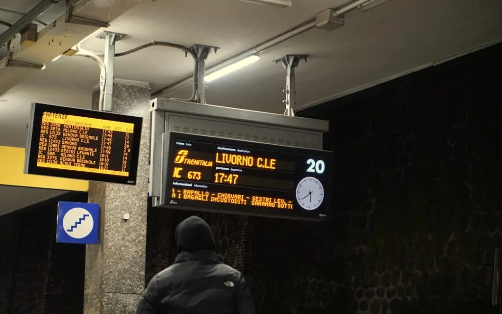 Quais de gare, tableau d'affichage indiquant LIVORNO C.LE et un passager