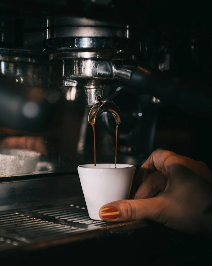 Ekspres do kawy nalewa espresso do filiżanki, widoczna dłoń
