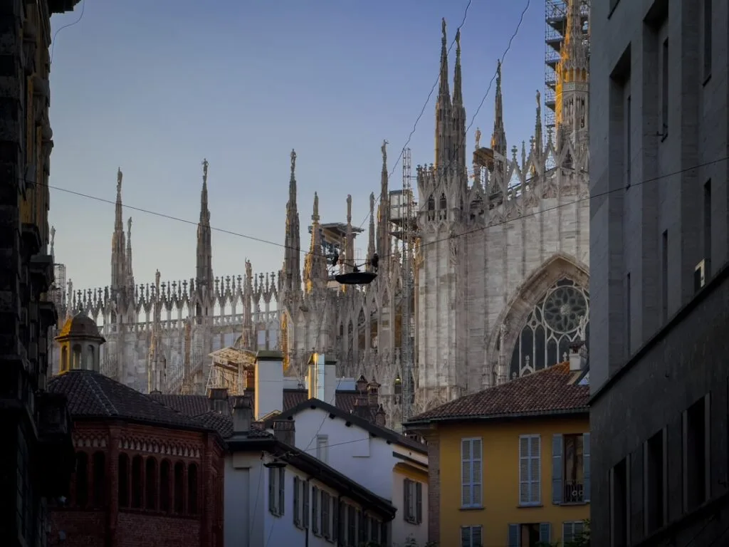 Flèche et façade du Duomo de Milan visible entre les toits
