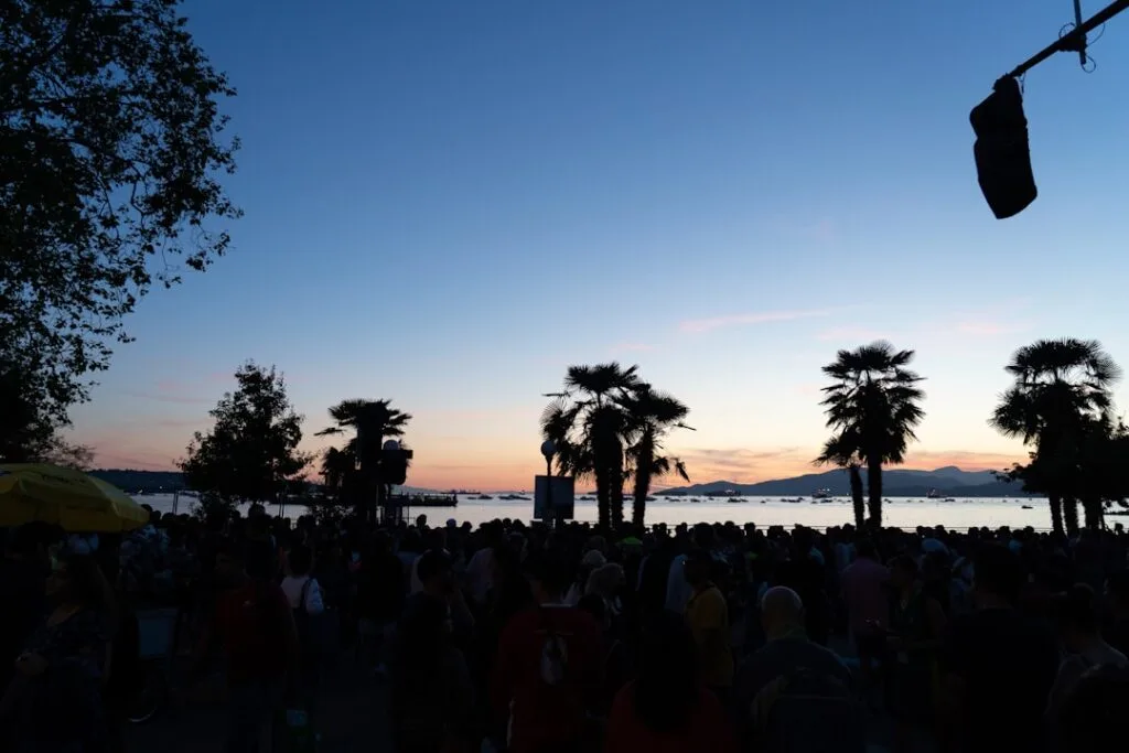 Foule au crépuscule devant des palmiers, horizon marin et bateaux