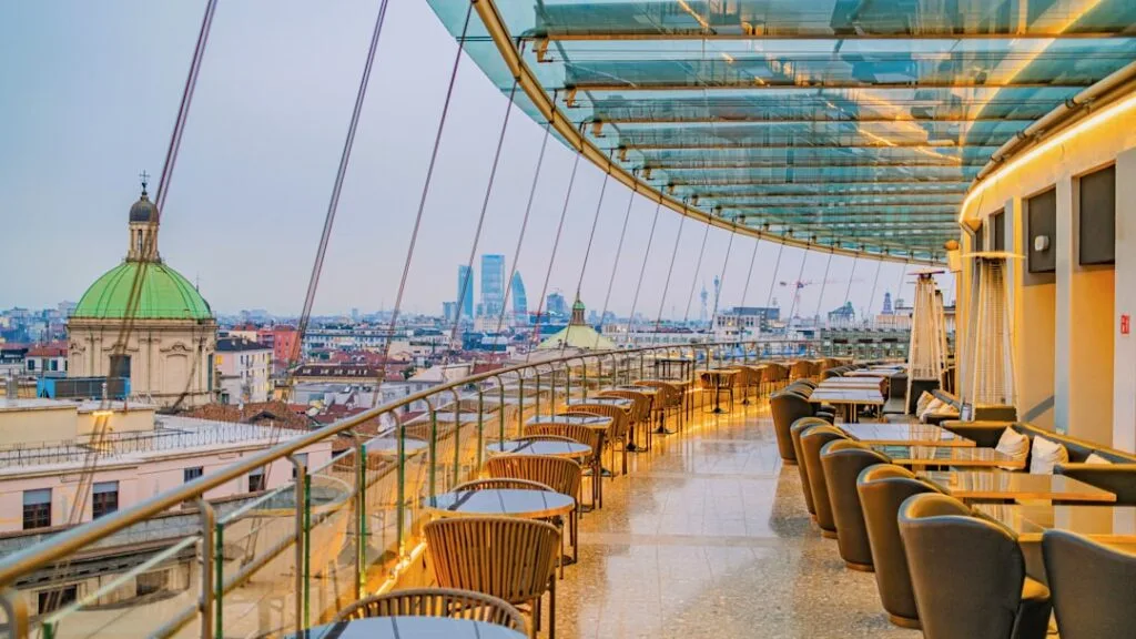 Terrasse rooftop avec tables et verrière offrant une vue sur Milan
