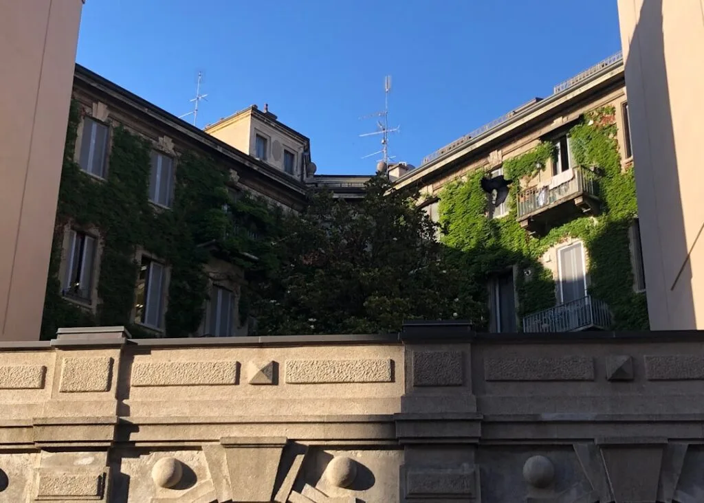 Façade recouverte de lierre et balcon d'un immeuble milanais sous ciel bleu