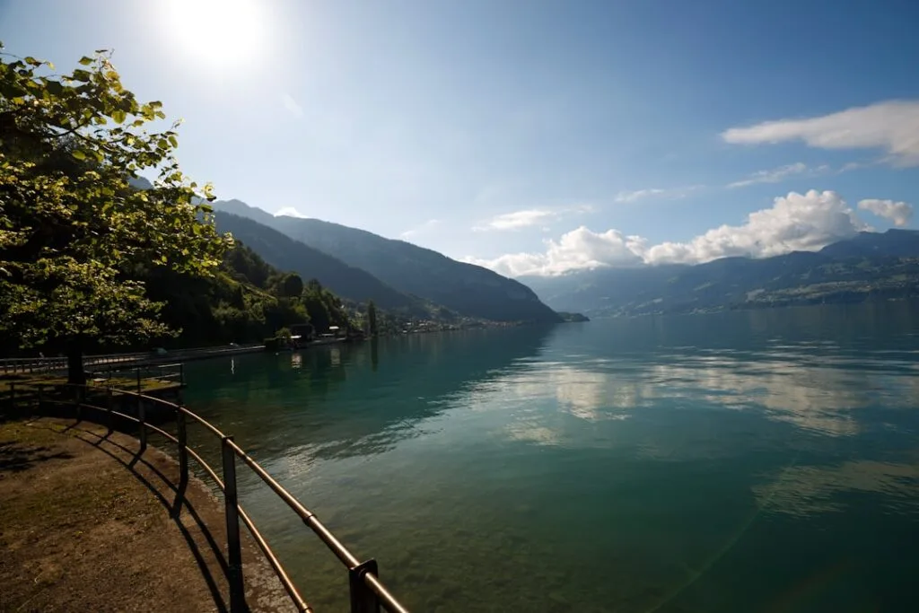 Promenade au bord du lac, montagnes et eau turquoise au loin.