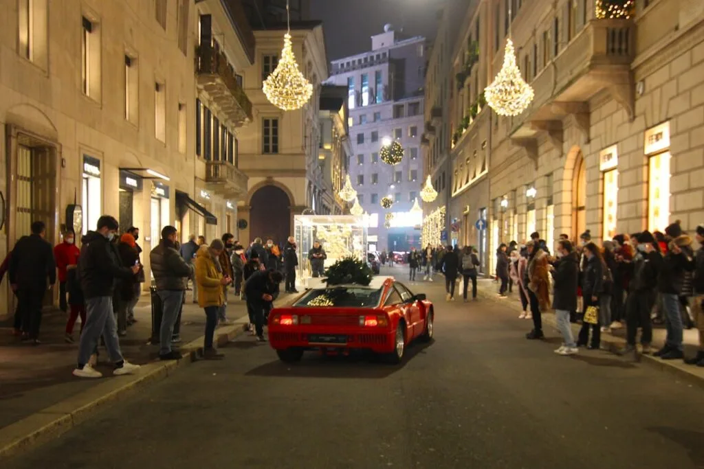 Voiture de sport rouge circulant dans une rue commerçante illuminée de Milan