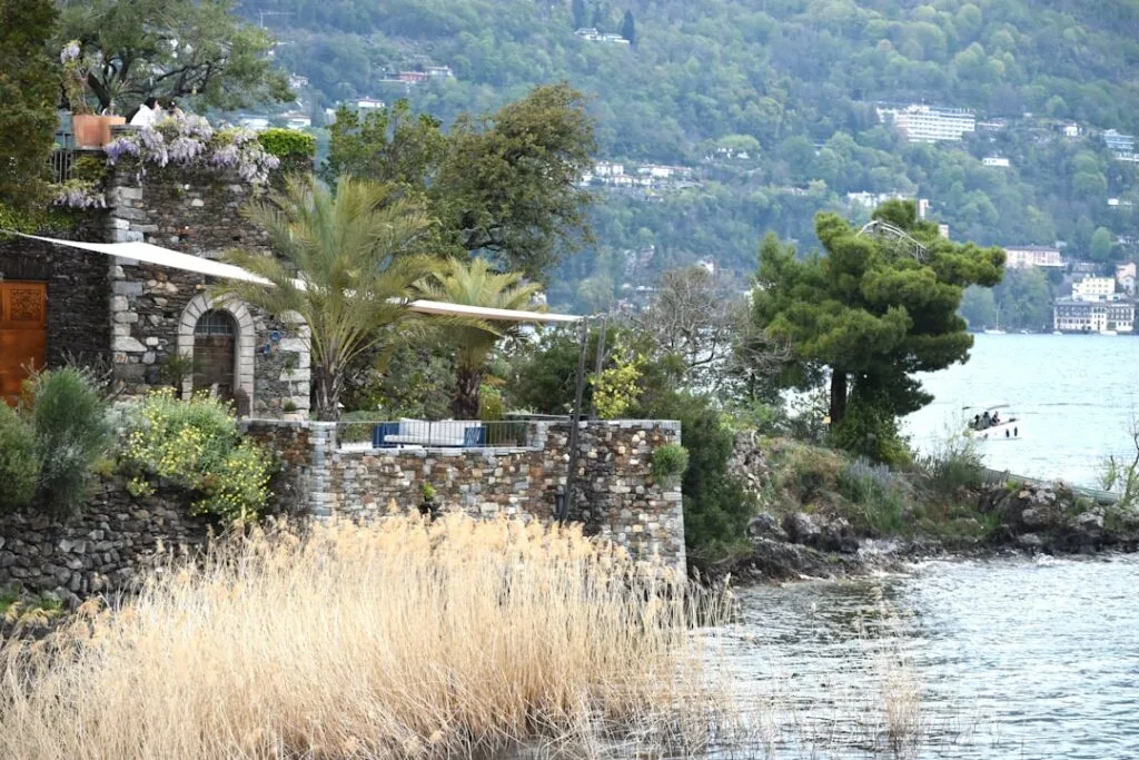Terrasse en pierre au bord du lac, roseaux et bateau au loin.