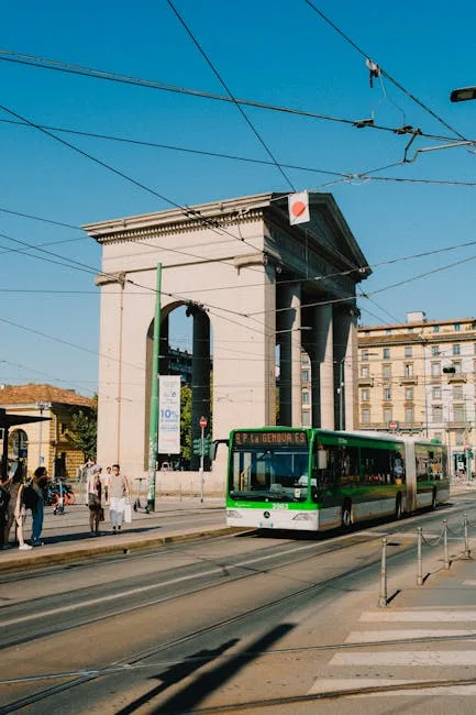 Monumentale boog en groene bus langs een levendige straat in Milaan