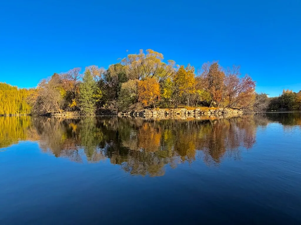 Klein boomrijk eiland met herfstkleuren en spiegeling in rustig water