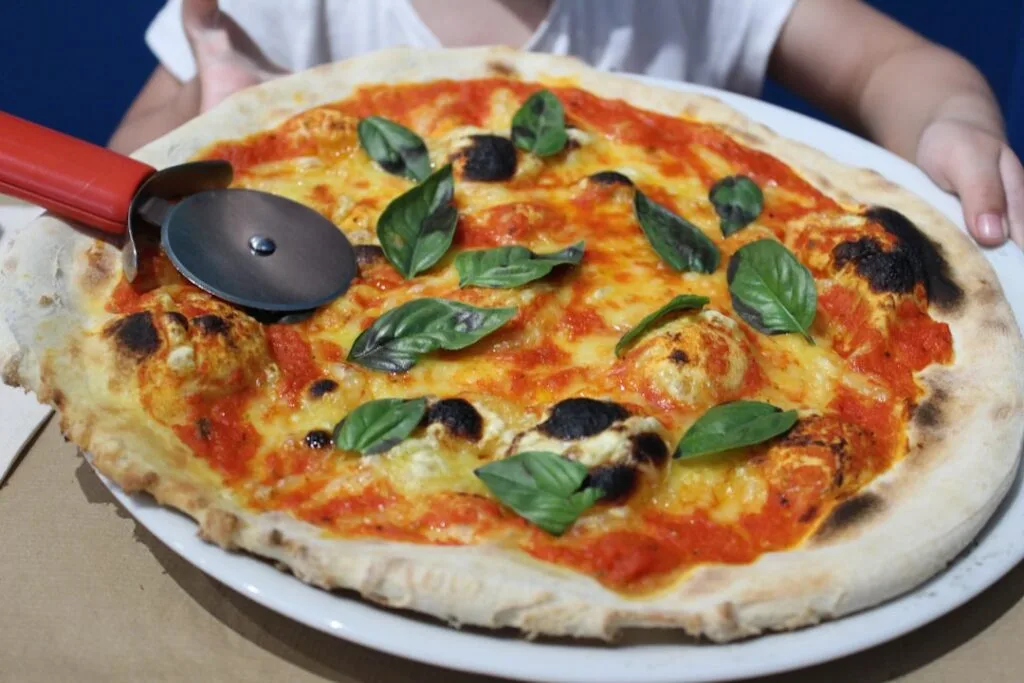Charred Neapolitan margherita pizza with basil and pizza cutter on plate