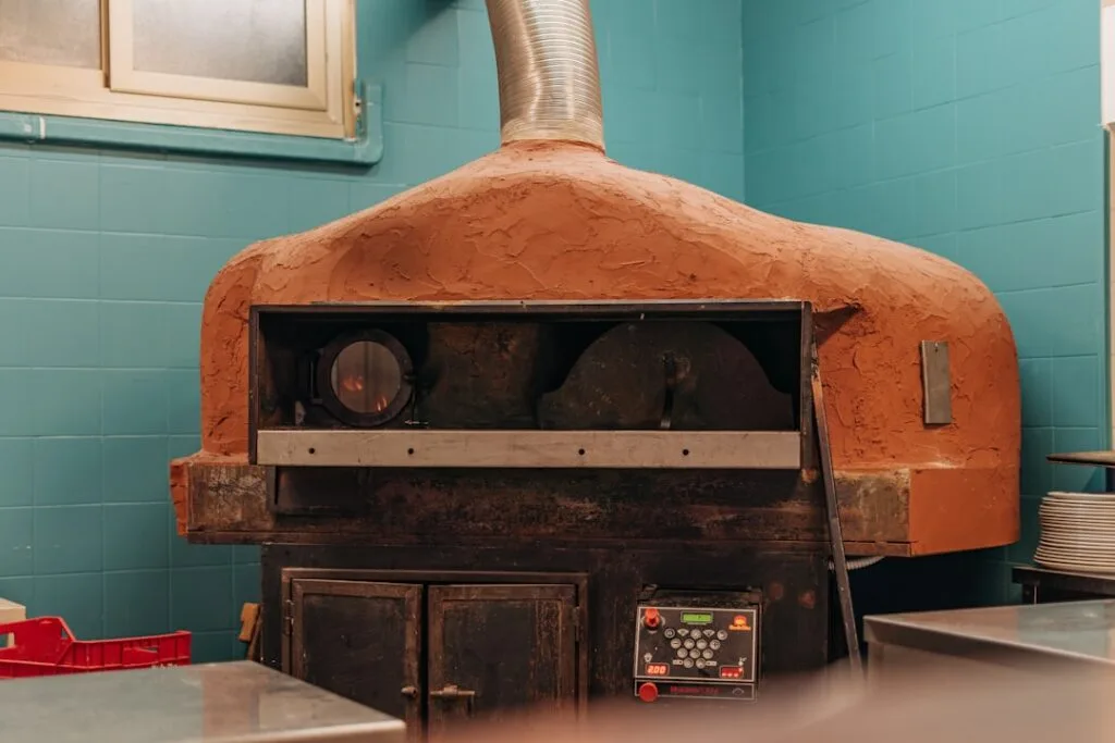 Terracotta-domed pizza oven against turquoise tiles inside a Naples pizzeria