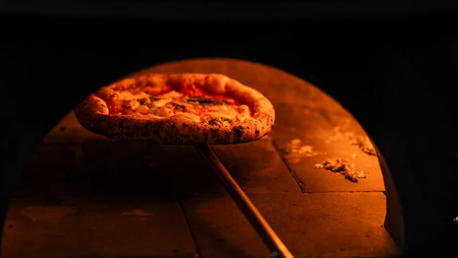 Neapolitan pizza on a peel browning inside a wood-fired oven