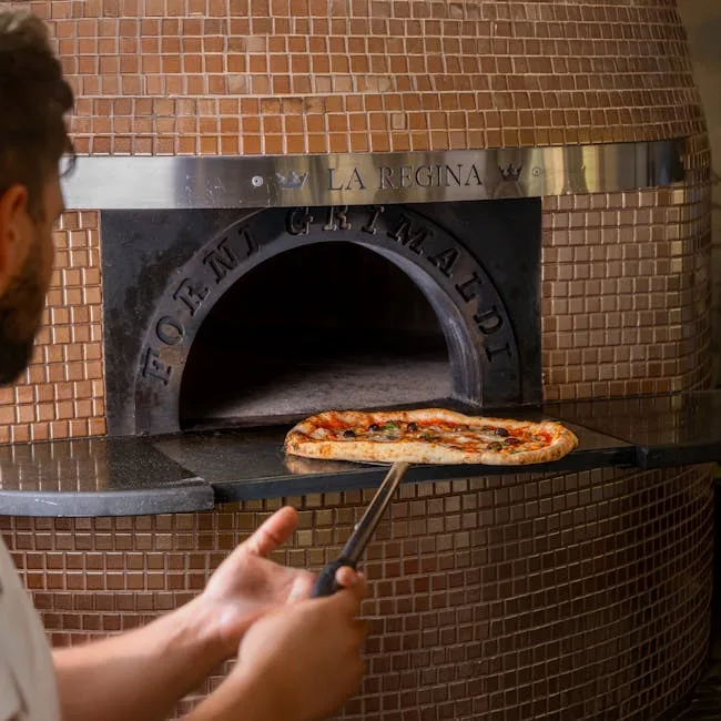 Baker sliding a Neapolitan pizza from tiled wood-fired oven