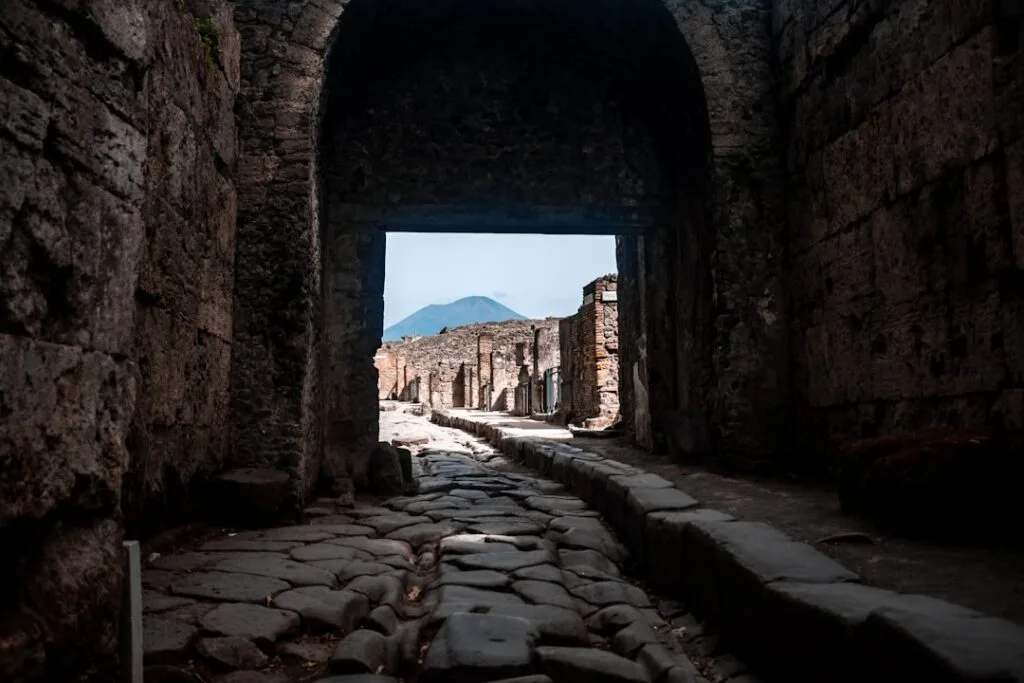 Ancient Pompeii street framed by archway with Mount Vesuvius visible.