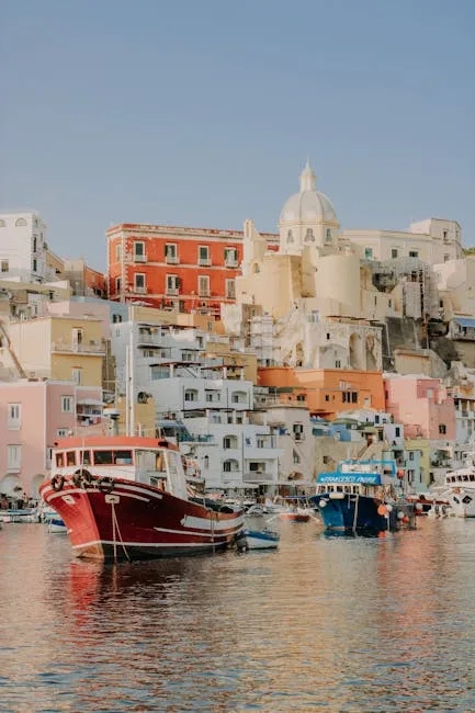 Red and blue fishing boats moored before pastel Procida houses and church dome