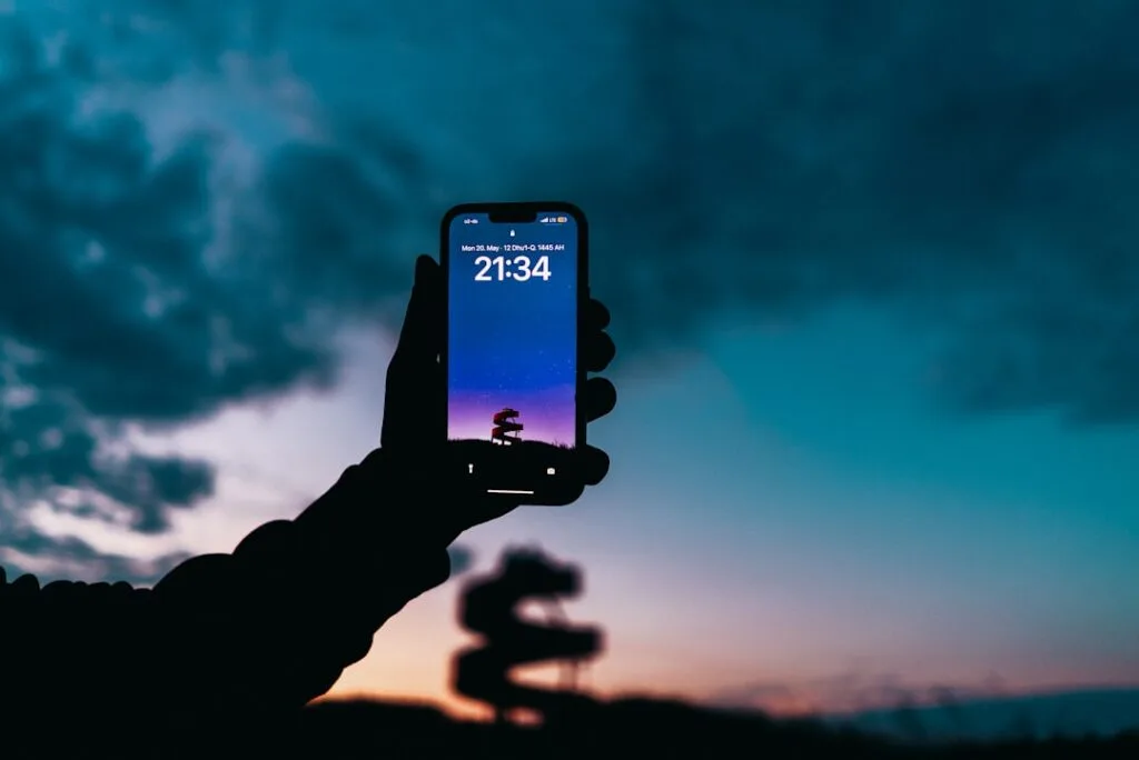 Silhouetted hand holding phone showing 21:34 against twilight sky