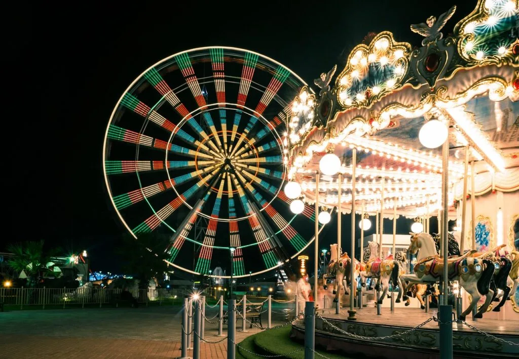 Illuminated Ferris wheel and carousel at a Naples seaside amusement park.