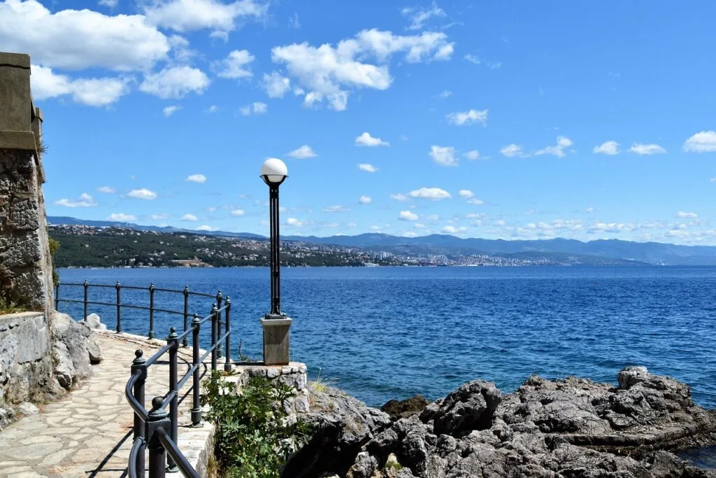 Seafront promenade and lamp post along Naples coastline with distant hills
