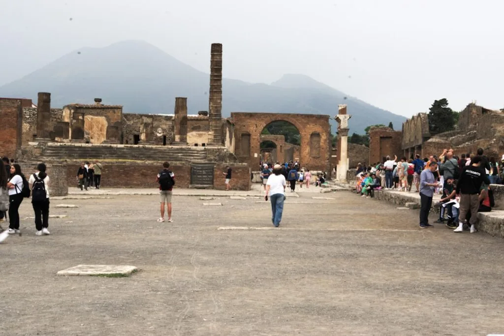 Tourists walking through Pompeii forum ruins with Mount Vesuvius backdrop