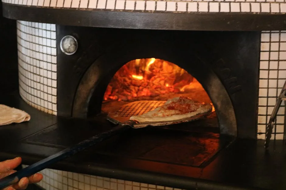 Holzofen in Neapel mit Pizza auf Schaufel vor brennendem Feuer