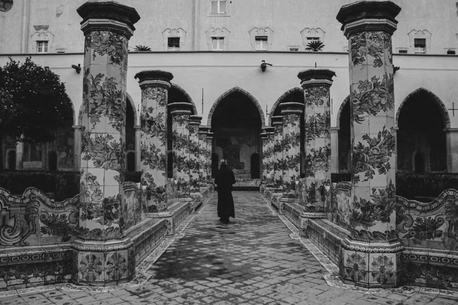 Schwarzweißes Bild vom Klosterhof in Neapel mit bemalten Säulen und Person.