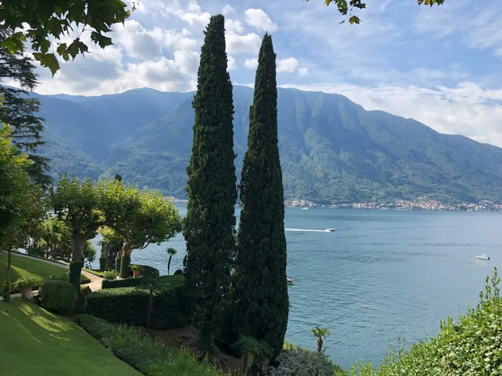 Gepflegter Garten mit zwei Zypressen, die den Comer See und Boote überragen