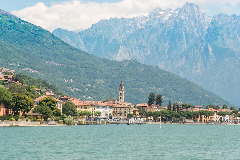 Ortsufer mit Kirchturm und Bergen am Comer See, ruhiges Wasser.