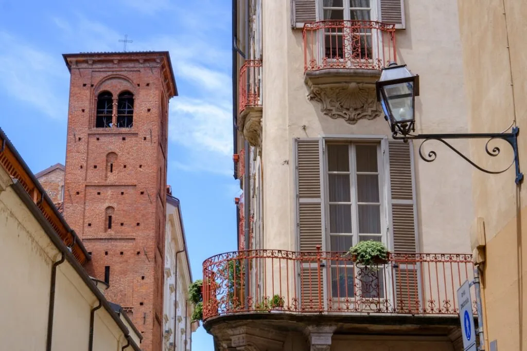 Façade claire avec balcon en fer forgé et clocher brique en arrière.