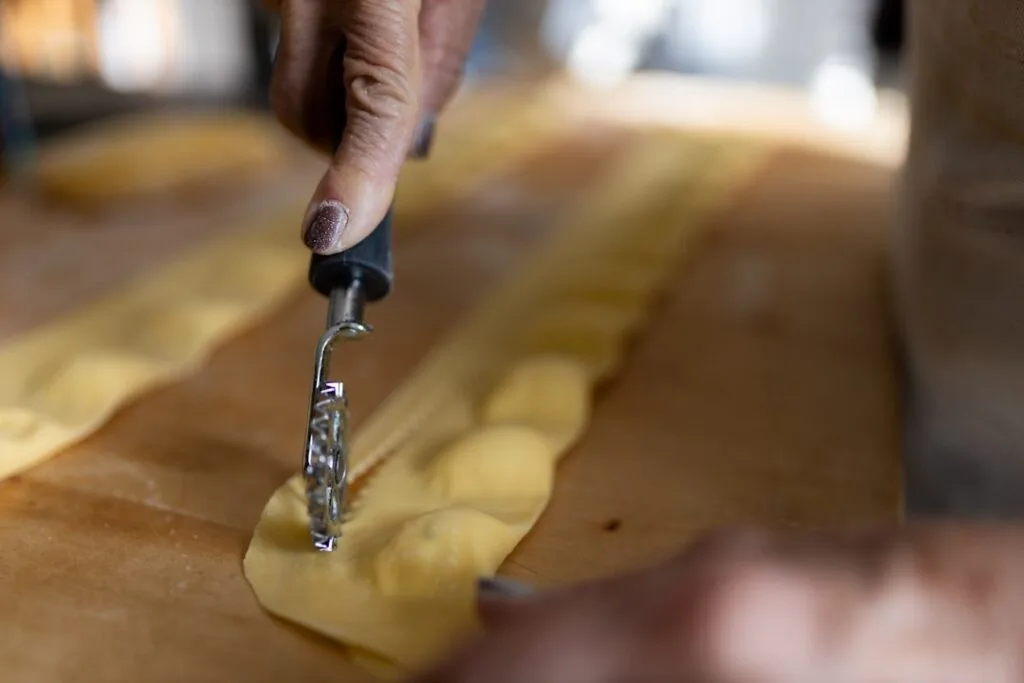 Main qui découpe des raviolis maison à l'aide d'une roulette à San Gimignano