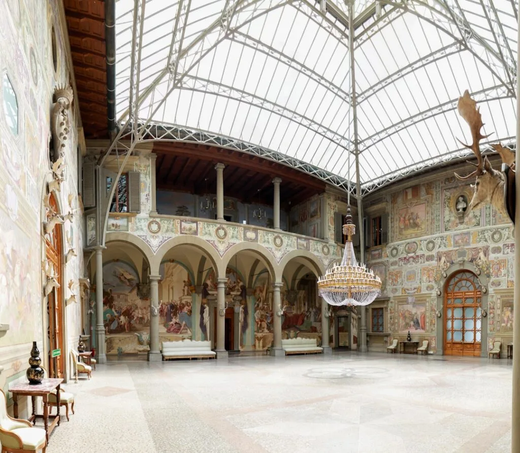 Grande cour intérieure vitrée ornée de fresques et lustre.