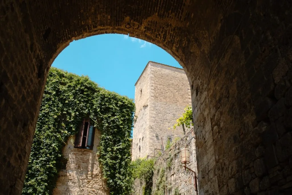 Vue en arche sur tour et façade végétalisée à San Gimignano