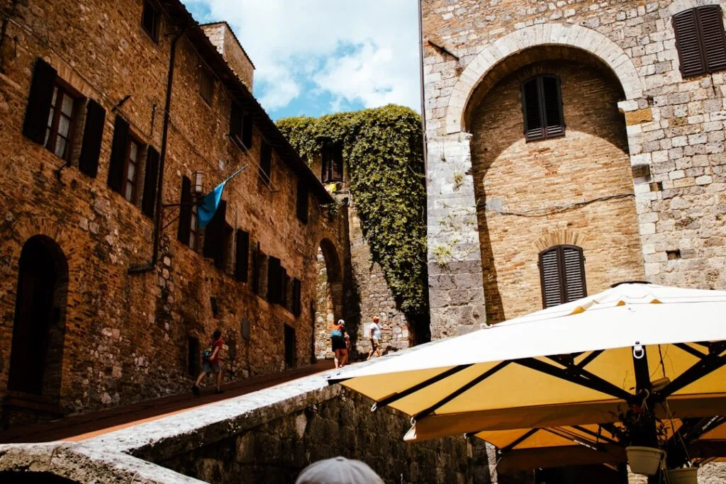 Ruelle pavée de San Gimignano avec parasol et passants montant
