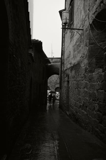 Narrow shadowed alley in San Gimignano with silhouetted pedestrians walking