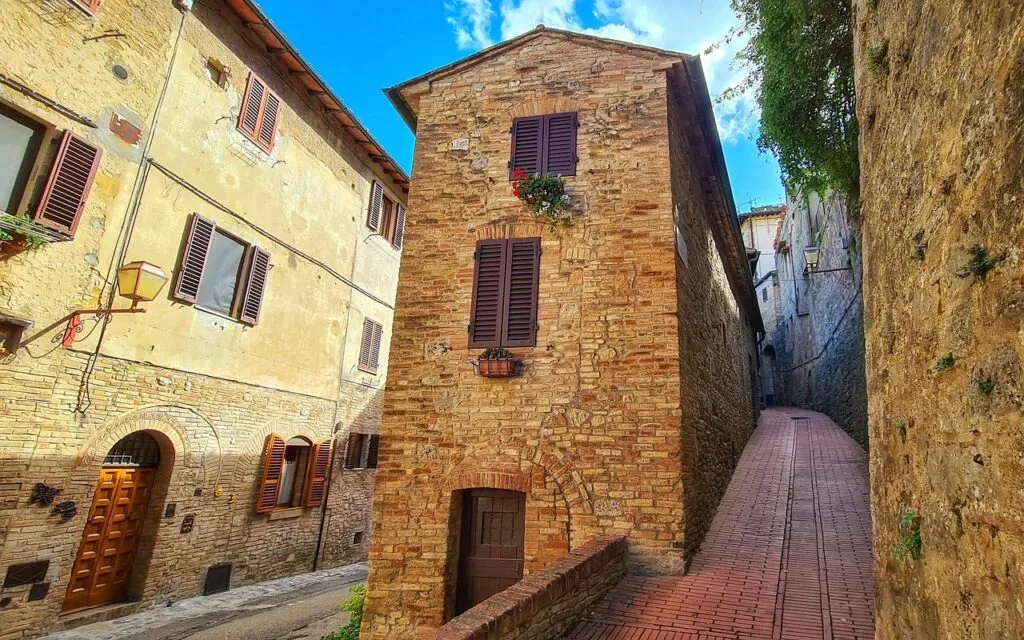 Kleine bakstenen steeg in San Gimignano met houten luiken en bloembak